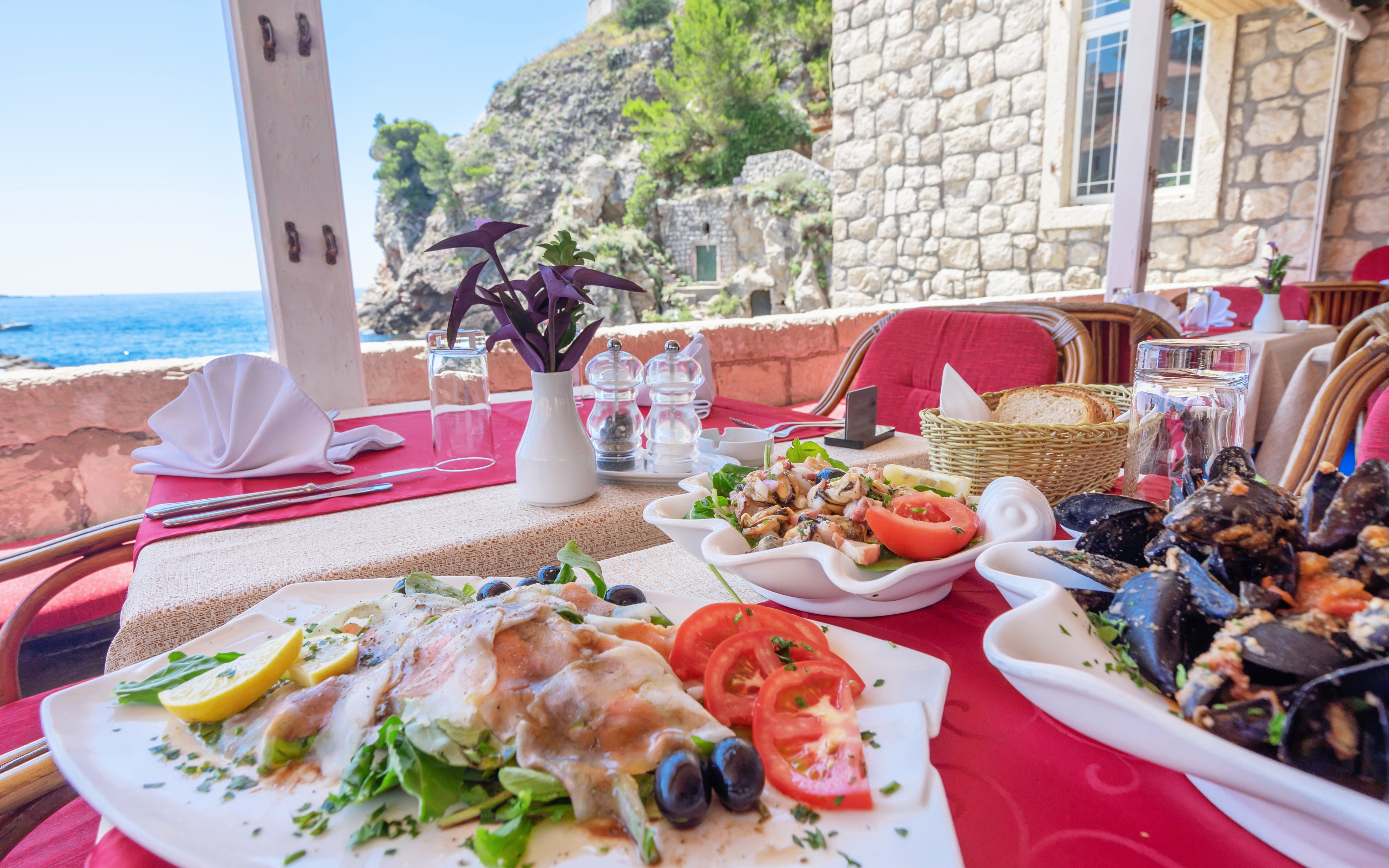 Seafood dishes on a table with ocean view at a Dubrovnik restaurant, Croatia.