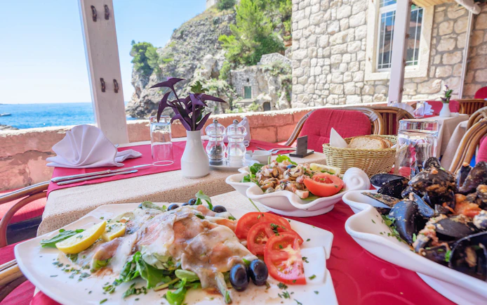 Seafood dishes on a table with ocean view at a Dubrovnik restaurant, Croatia.