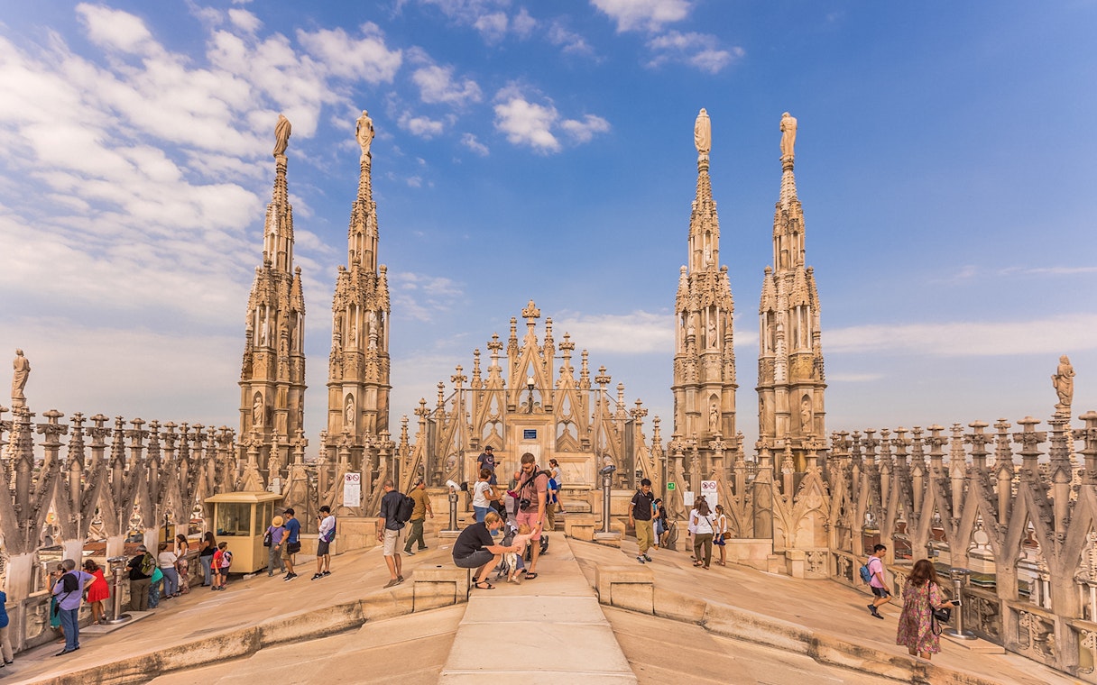 Visitors exploring the rooftop spires of Milan Duomo Cathedral under a clear sky.