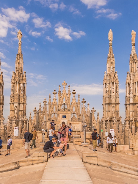 Visitors exploring the rooftop spires of Milan Duomo Cathedral under a clear sky.