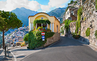 Positano coastal road with hillside houses and scenic mountain backdrop.