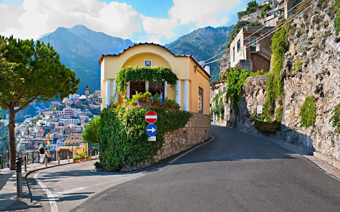 Positano coastal road with hillside houses and scenic mountain backdrop.