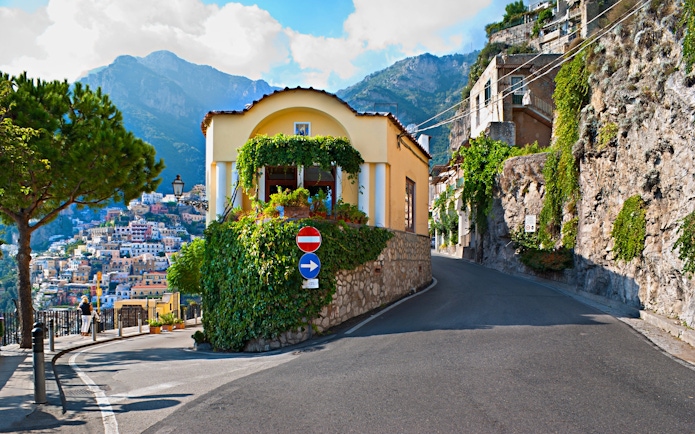 Positano coastal road with hillside houses and scenic mountain backdrop.