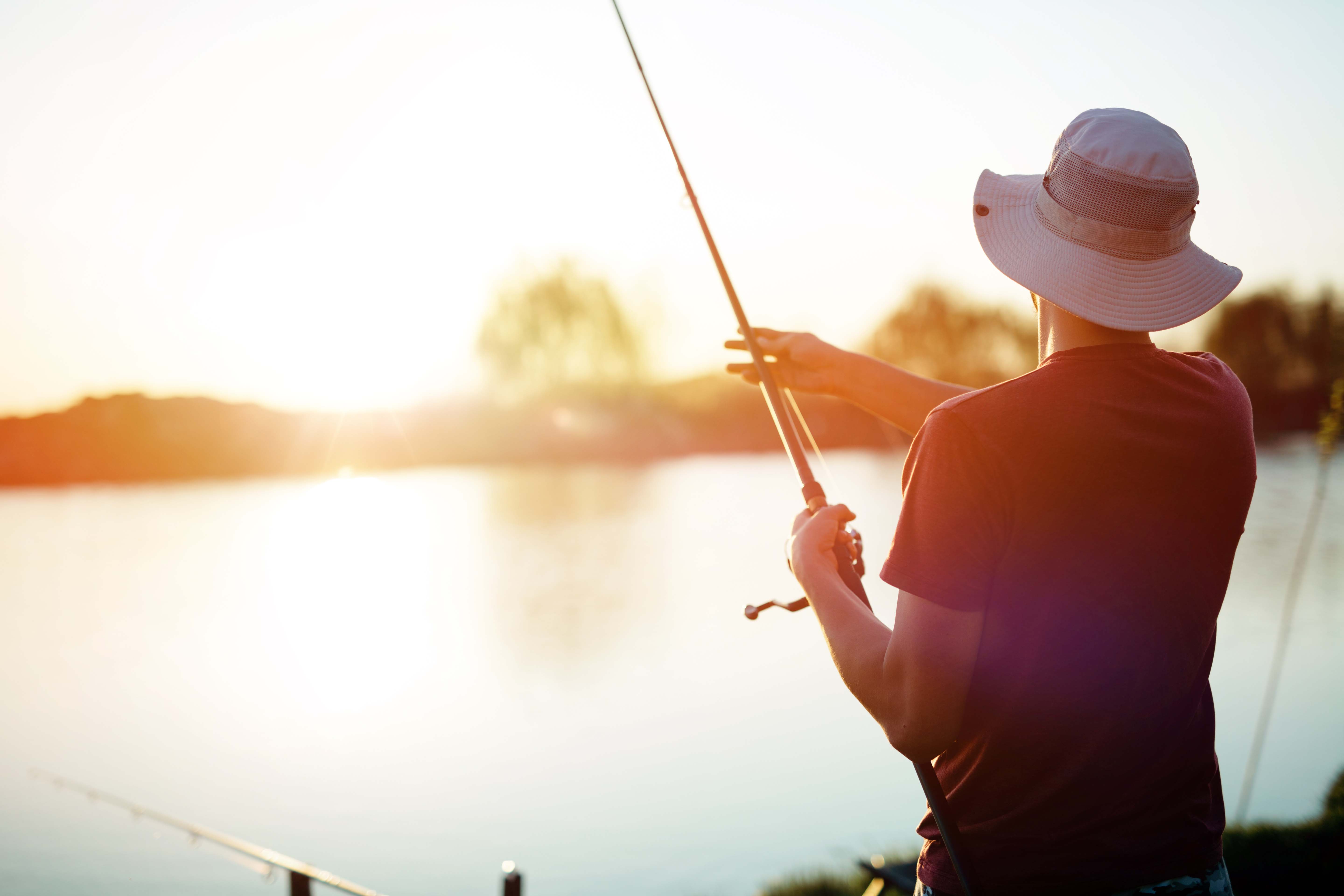 Person fishing at a lake during sunset.