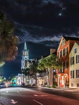 Charleston street at night with historic buildings and church steeple.