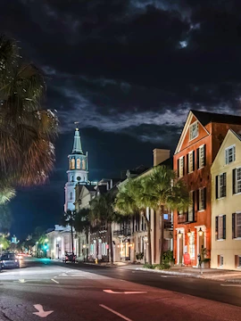 Charleston street at night with historic buildings and church steeple.