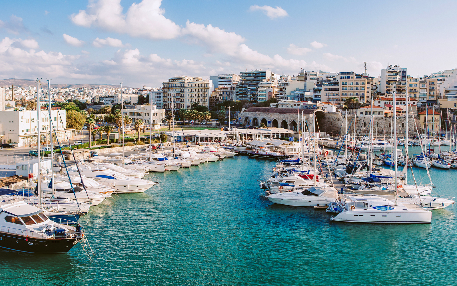 Heraklion marina with yachts and cityscape, part of the Hop-On Hop-Off Sightseeing Bus Tour.