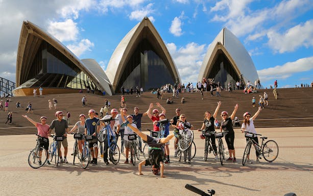 Group of bikers posing with bicycles in front of Sydney Opera House.