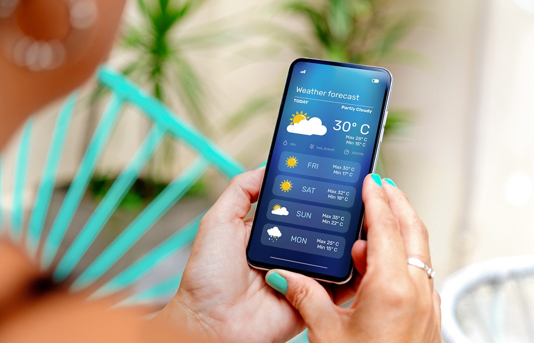 A person checking out a weather forecast app on her mobile phone at home.