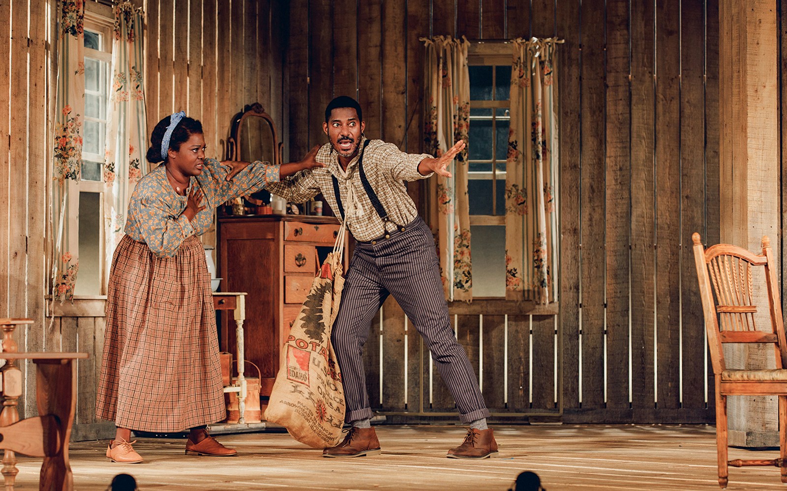 Two actors perform a scene from "Purlie Victorious" in a rustic wooden room.