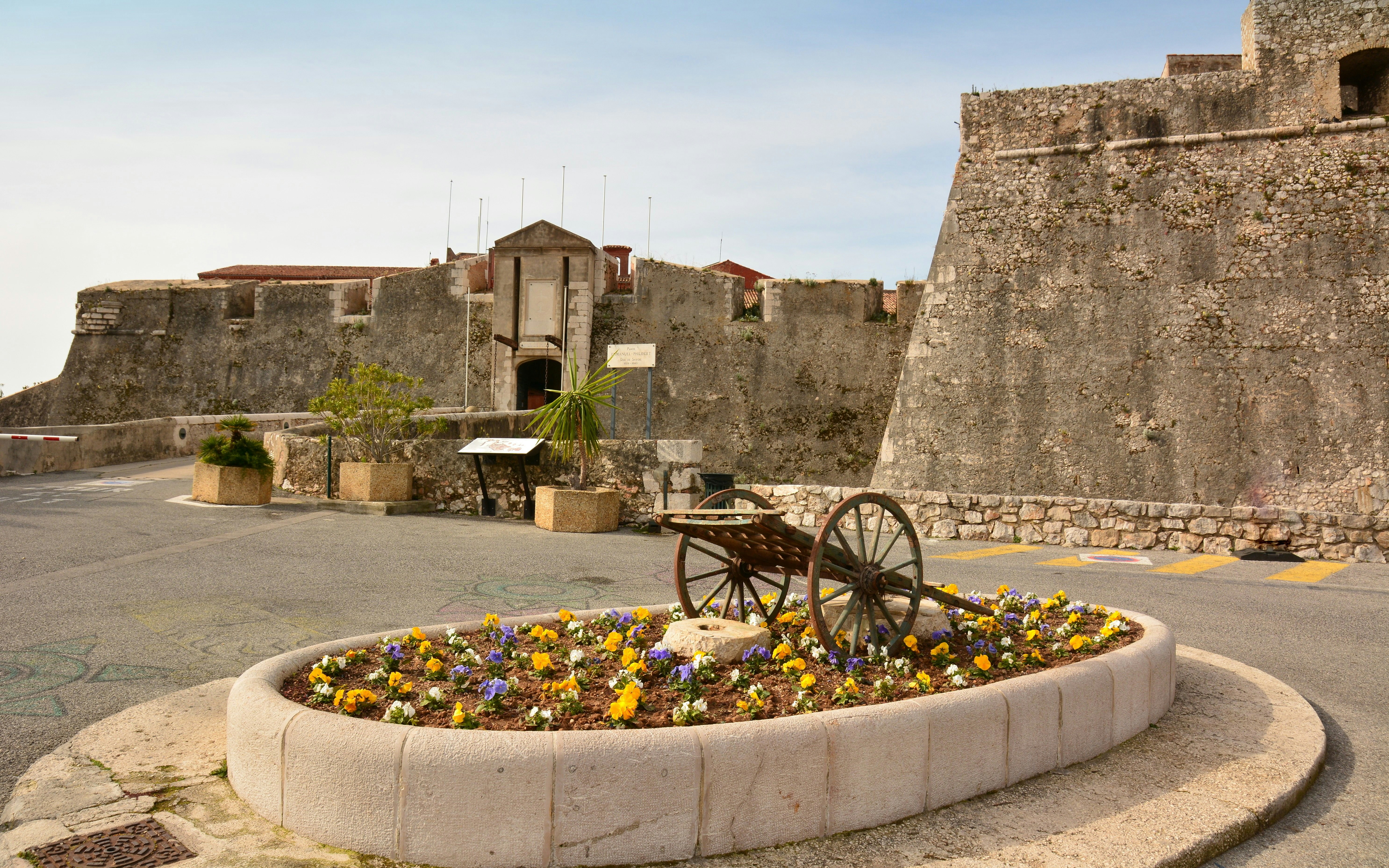 Historischer Festungseingang mit Blumenbeet und altem Wagenrad in Villefranche-sur-Mer, Nizza.