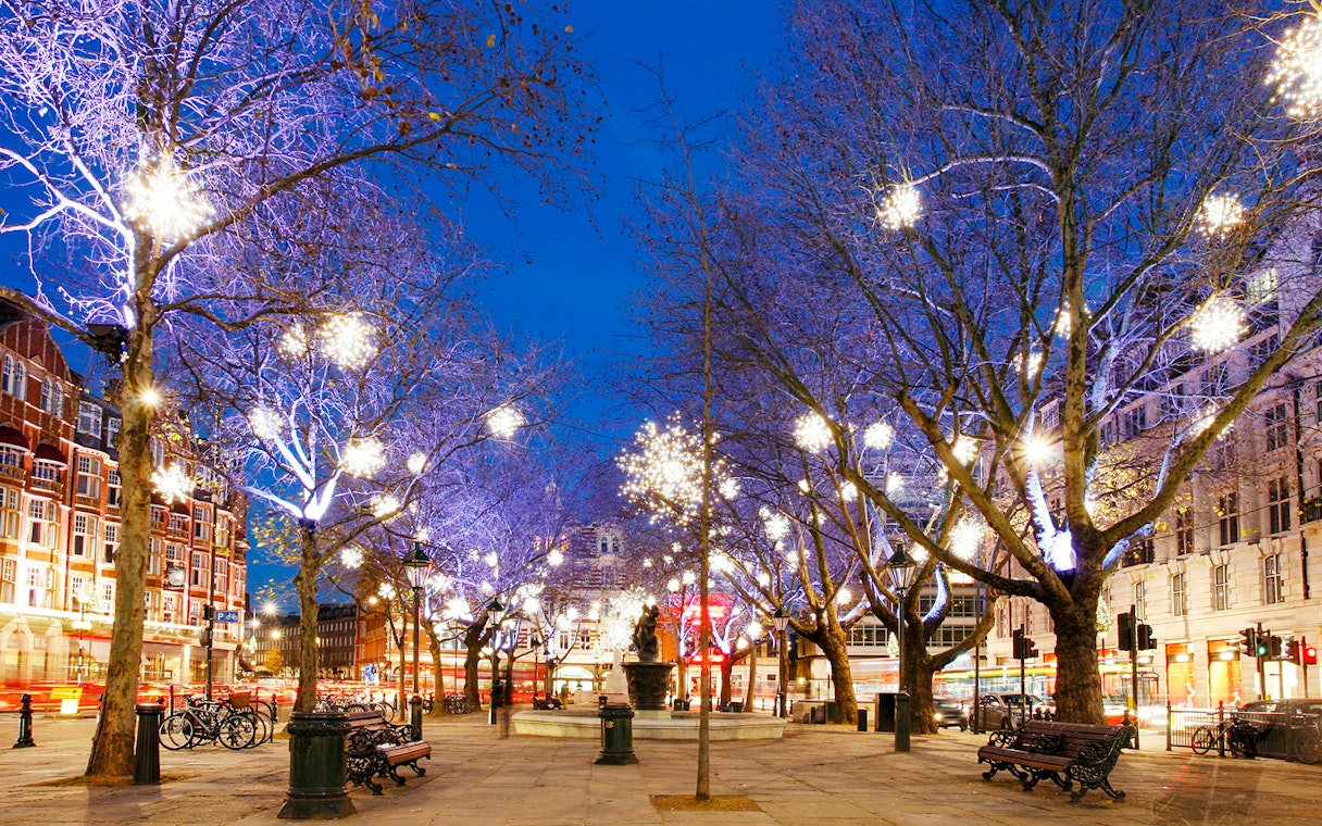 London street adorned with festive Christmas lights on trees during evening tour.