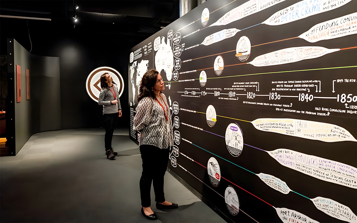 Visitors exploring historical timeline exhibit at Port Arthur museum.