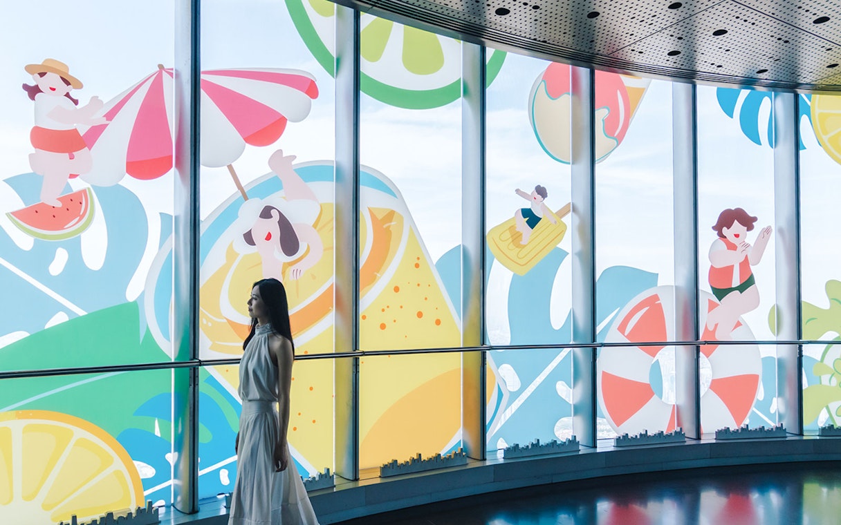 Woman walking past summer-themed cartoon decals on Shanghai Tower windows.