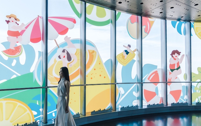 Woman walking past summer-themed cartoon decals on Shanghai Tower windows.