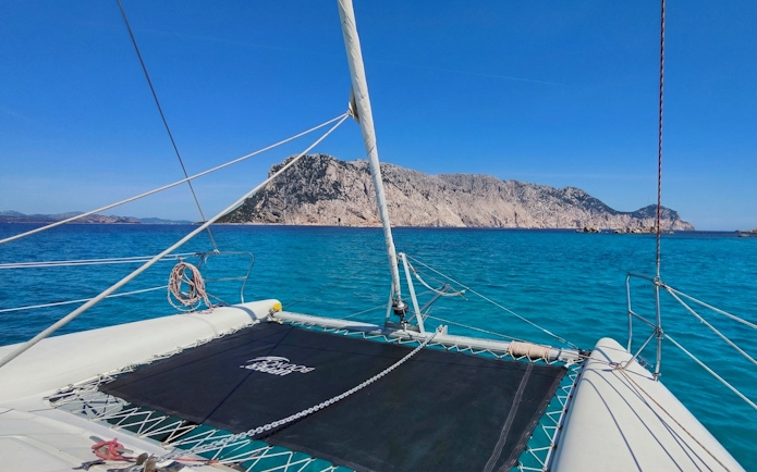 Catamaran sailing towards Tavolara Island, Sardinia, with clear blue waters.