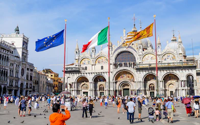 Crowd in front of St Mark's Basilica, Venice, with flags of Italy and EU.