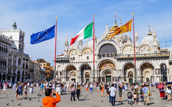 Crowd in front of St Mark's Basilica, Venice, with flags of Italy and EU.