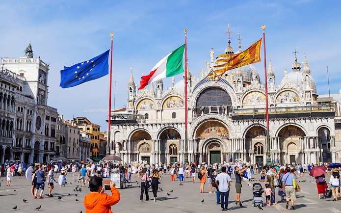 Crowd in front of St Mark's Basilica, Venice, with flags of Italy and EU.