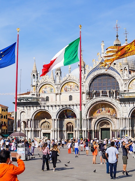 Crowd in front of St Mark's Basilica, Venice, with flags of Italy and EU.