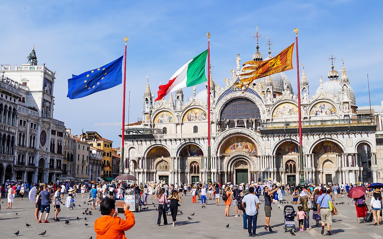 Crowd in front of St Mark's Basilica, Venice, with flags of Italy and EU.