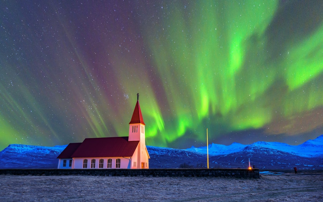 Church with red roof under vibrant northern lights in Iceland.