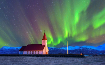 Church with red roof under vibrant northern lights in Iceland.