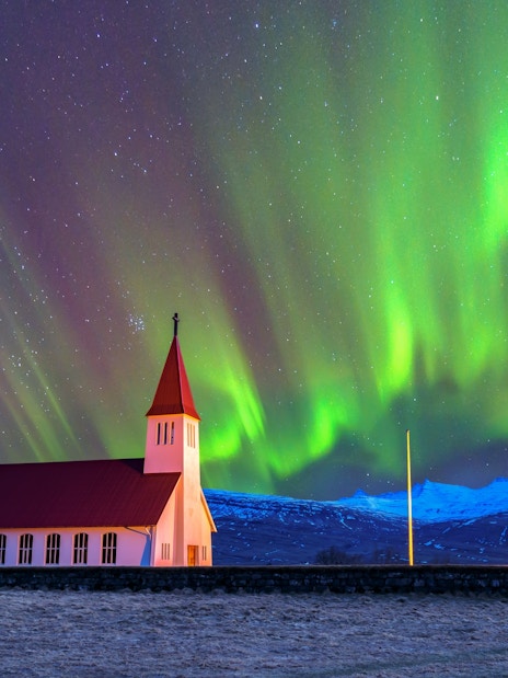 Church with red roof under vibrant northern lights in Iceland.