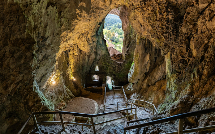 Interior view of Predjama Castle cave with rocky walls and a path leading outside, Slovenia.