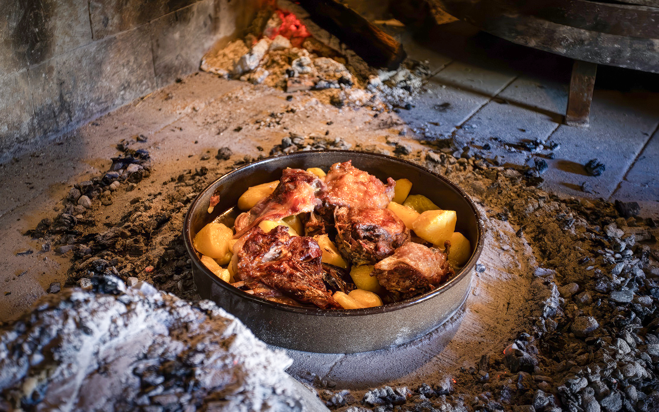 Traditional Croatian Peka dish with meat and potatoes cooking under hot coals.