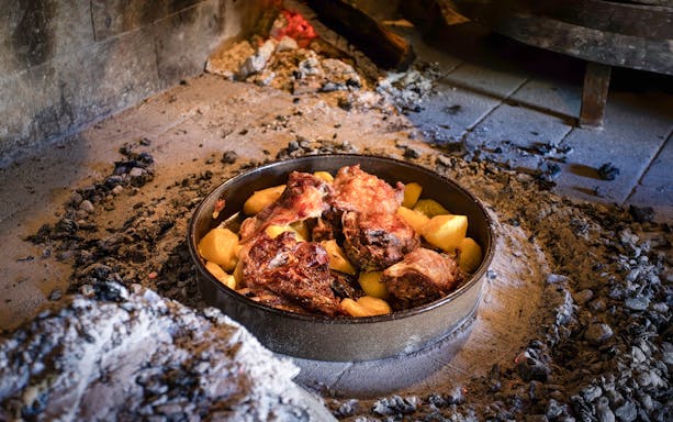 Traditional Croatian Peka dish with meat and potatoes cooking under hot coals.
