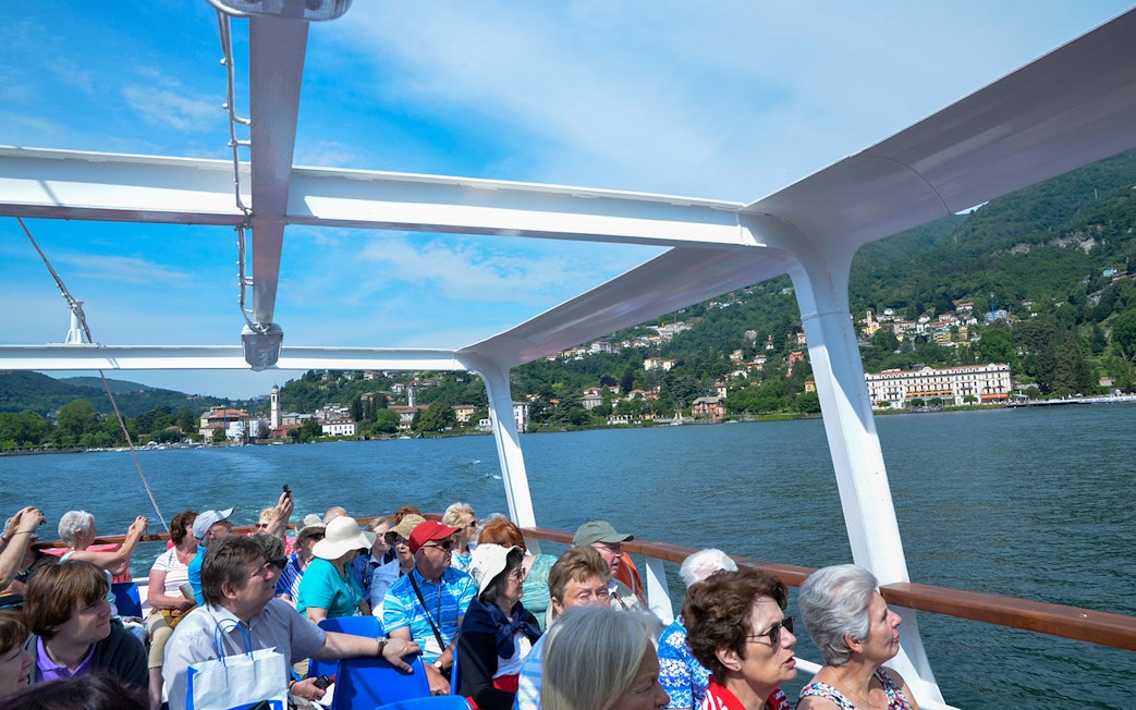 Tourists on a boat cruise enjoying views of Lake Como and surrounding villas.
