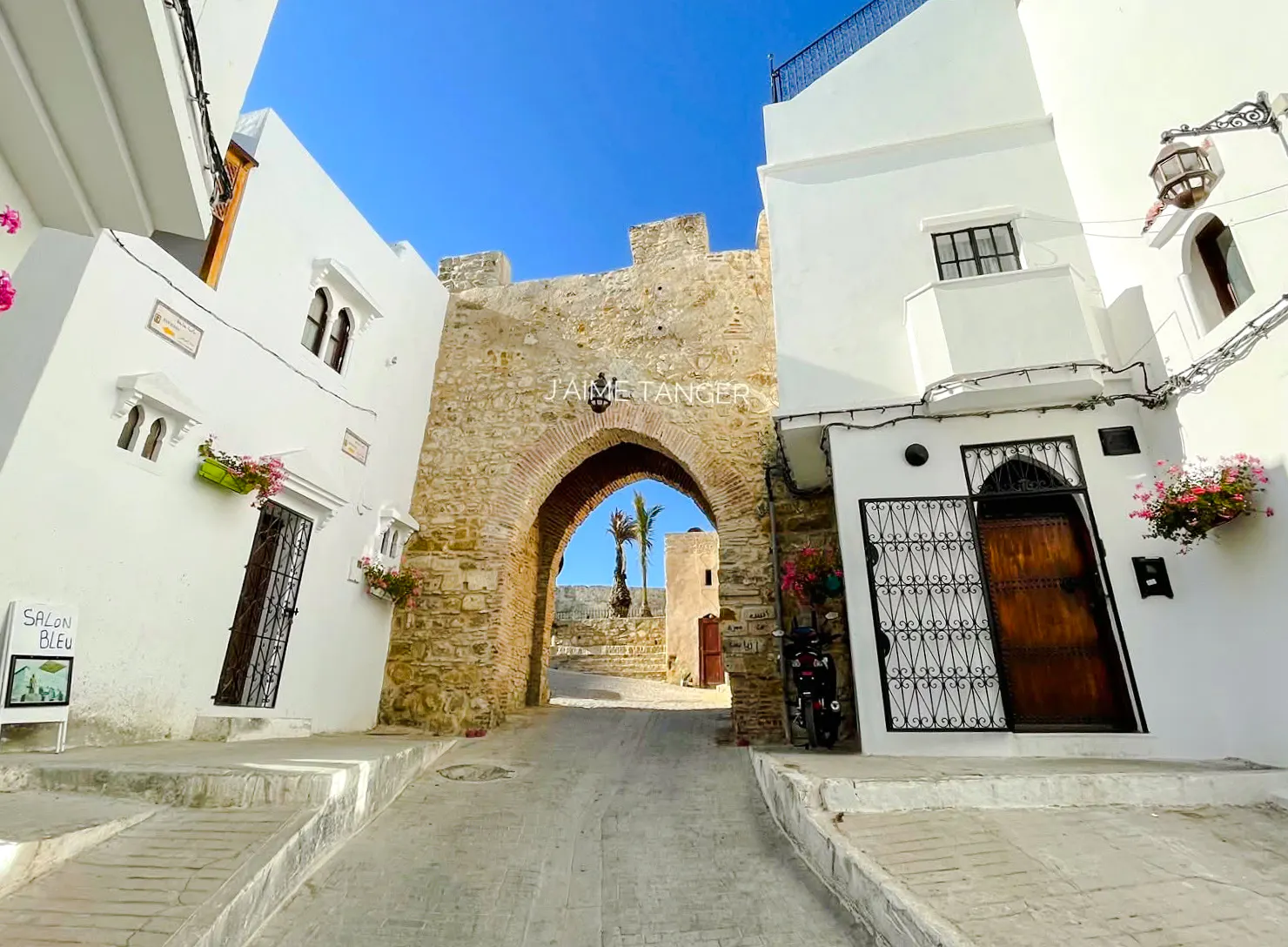 Stone archway entrance to Tangier's Medina with white buildings and cobblestone path.