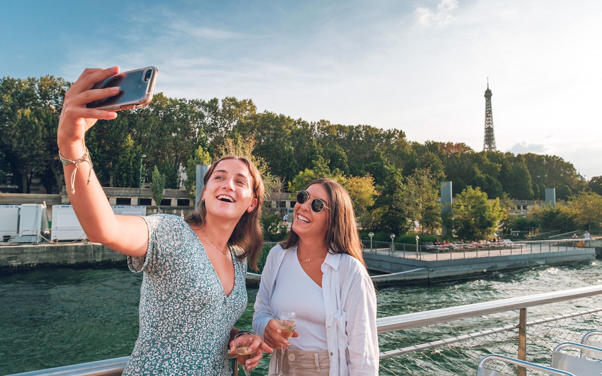 Two people taking a selfie on a Seine River cruise with the Eiffel Tower in the background.