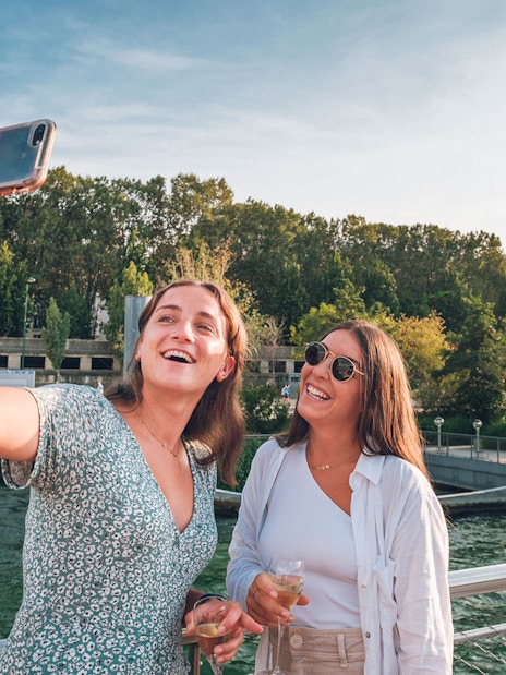 Two people taking a selfie on a Seine River cruise with the Eiffel Tower in the background.
