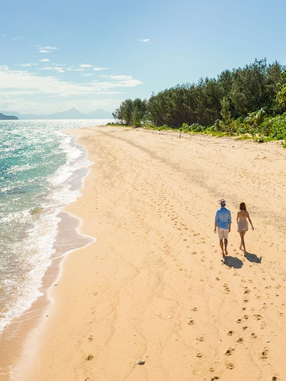 Couple walking on a sandy beach at Frankland Islands, with ocean and trees in the background.