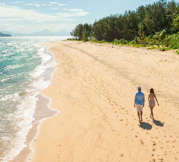 Couple walking on a sandy beach at Frankland Islands, with ocean and trees in the background.