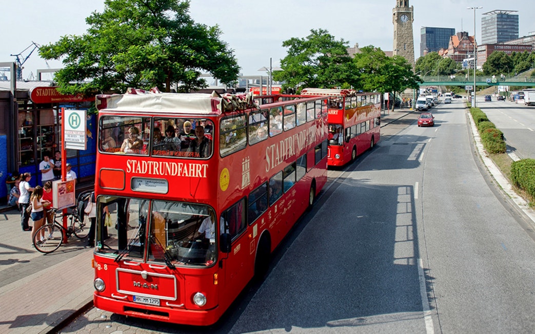 Red double-decker tour buses in Hamburg, Germany, near a clock tower, part of the Hamburg City Pass.