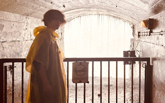 Person in yellow poncho near Niagara Falls tunnel with water cascading behind.