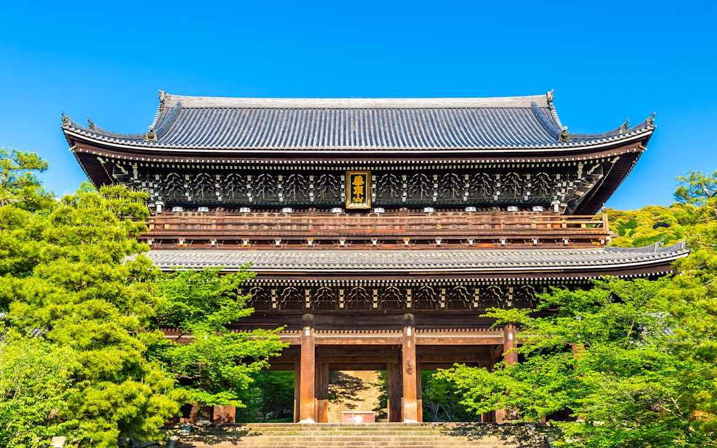Ancient wooden temple gate surrounded by lush greenery in Kyoto, Japan.