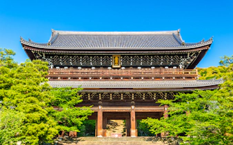 Ancient wooden temple gate surrounded by lush greenery in Kyoto, Japan.
