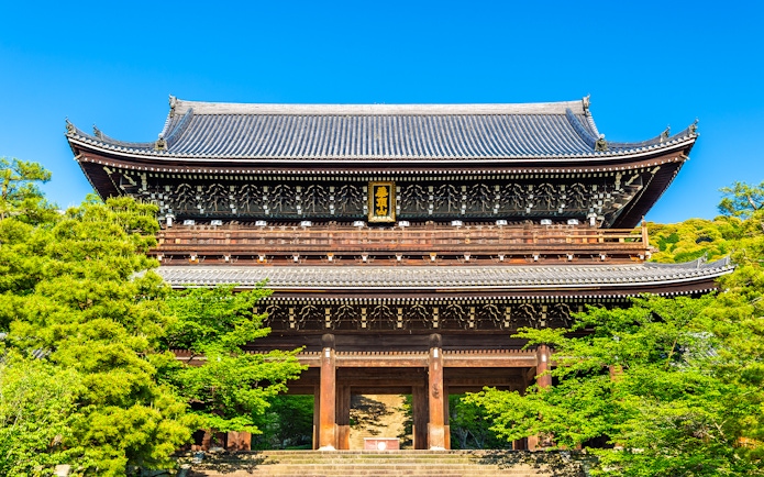 Ancient wooden temple gate surrounded by lush greenery in Kyoto, Japan.