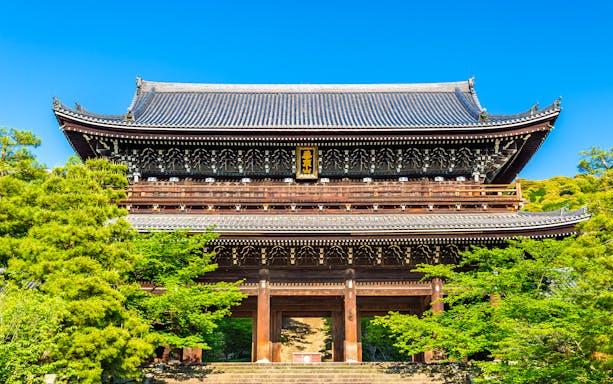 Ancient wooden temple gate surrounded by lush greenery in Kyoto, Japan.