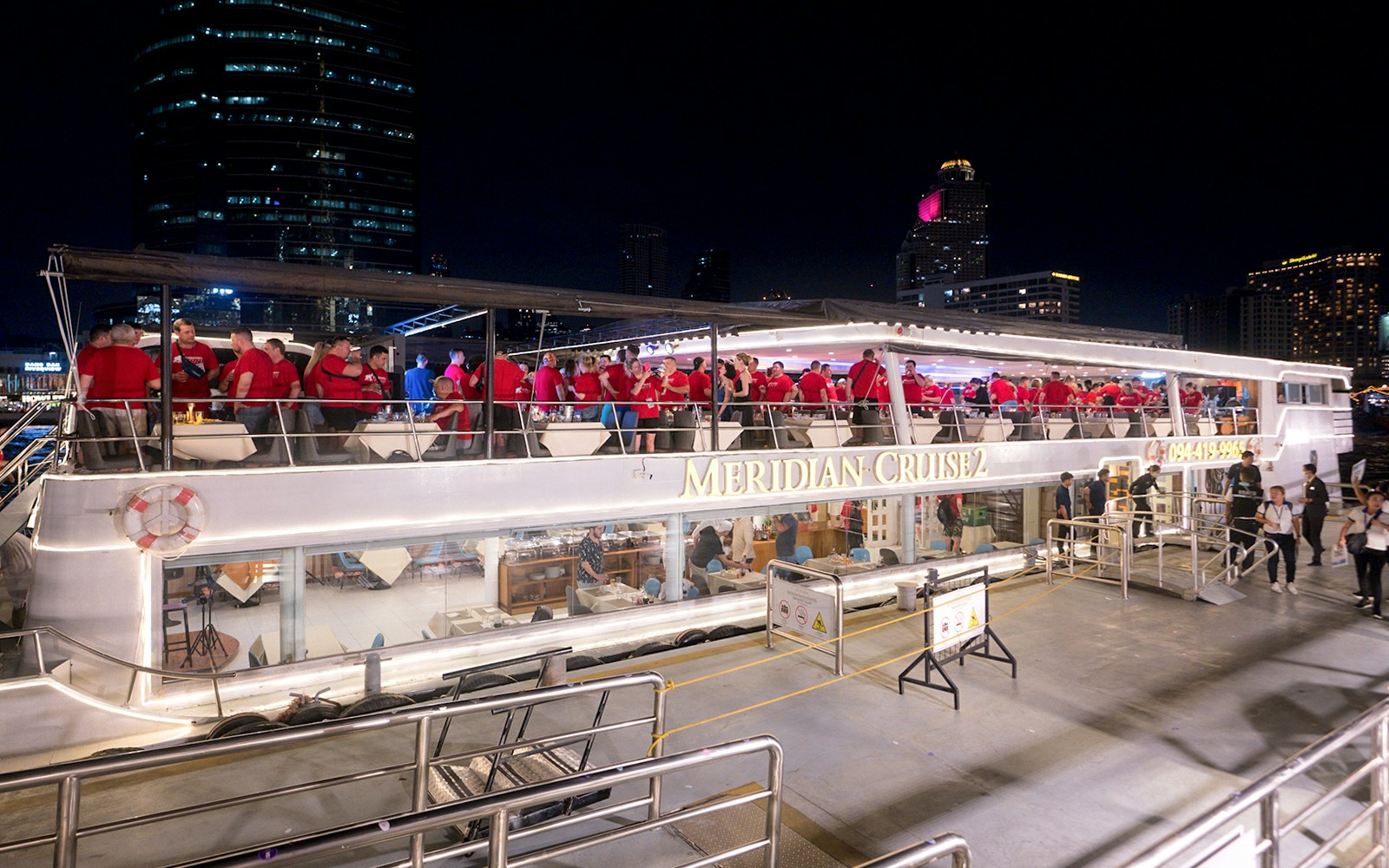 Meridian Cruise guests dining on a boat with Bangkok skyline in the background.