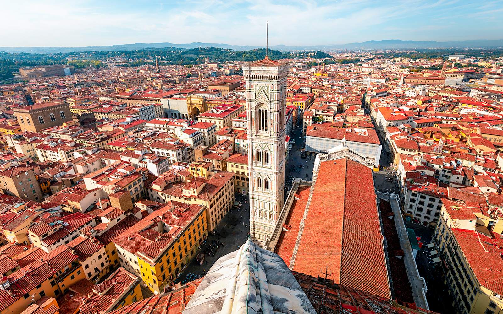 Aerial view of Florence cityscape from the Duomo, featuring Giotto's Campanile and red-tiled rooftops.