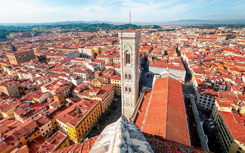 Aerial view of Florence cityscape from the Duomo, featuring Giotto's Campanile and red-tiled rooftops.
