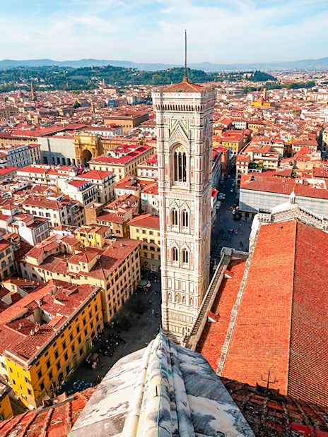 Aerial view of Florence cityscape from the Duomo, featuring Giotto's Campanile and red-tiled rooftops.