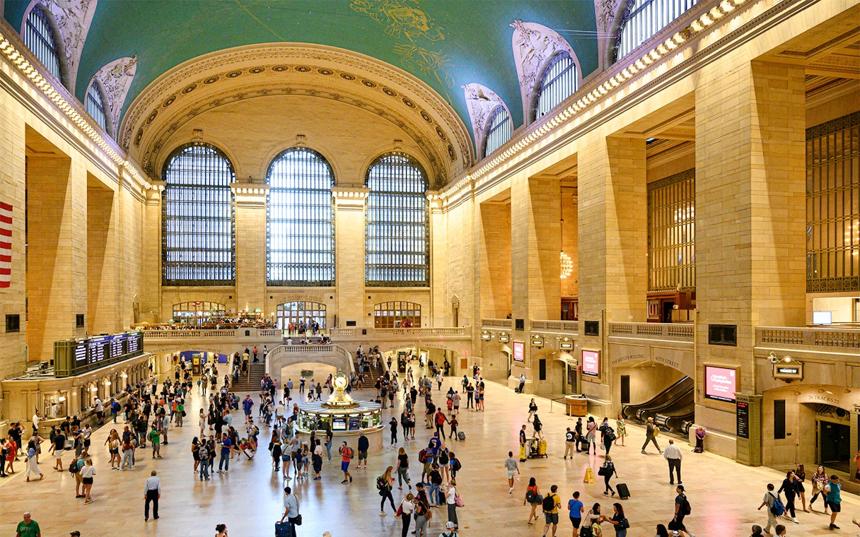 Crowd walking inside Grand Central Station, New York, with iconic arched windows and clock.