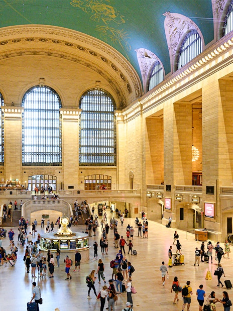 Crowd walking inside Grand Central Station, New York, with iconic arched windows and clock.