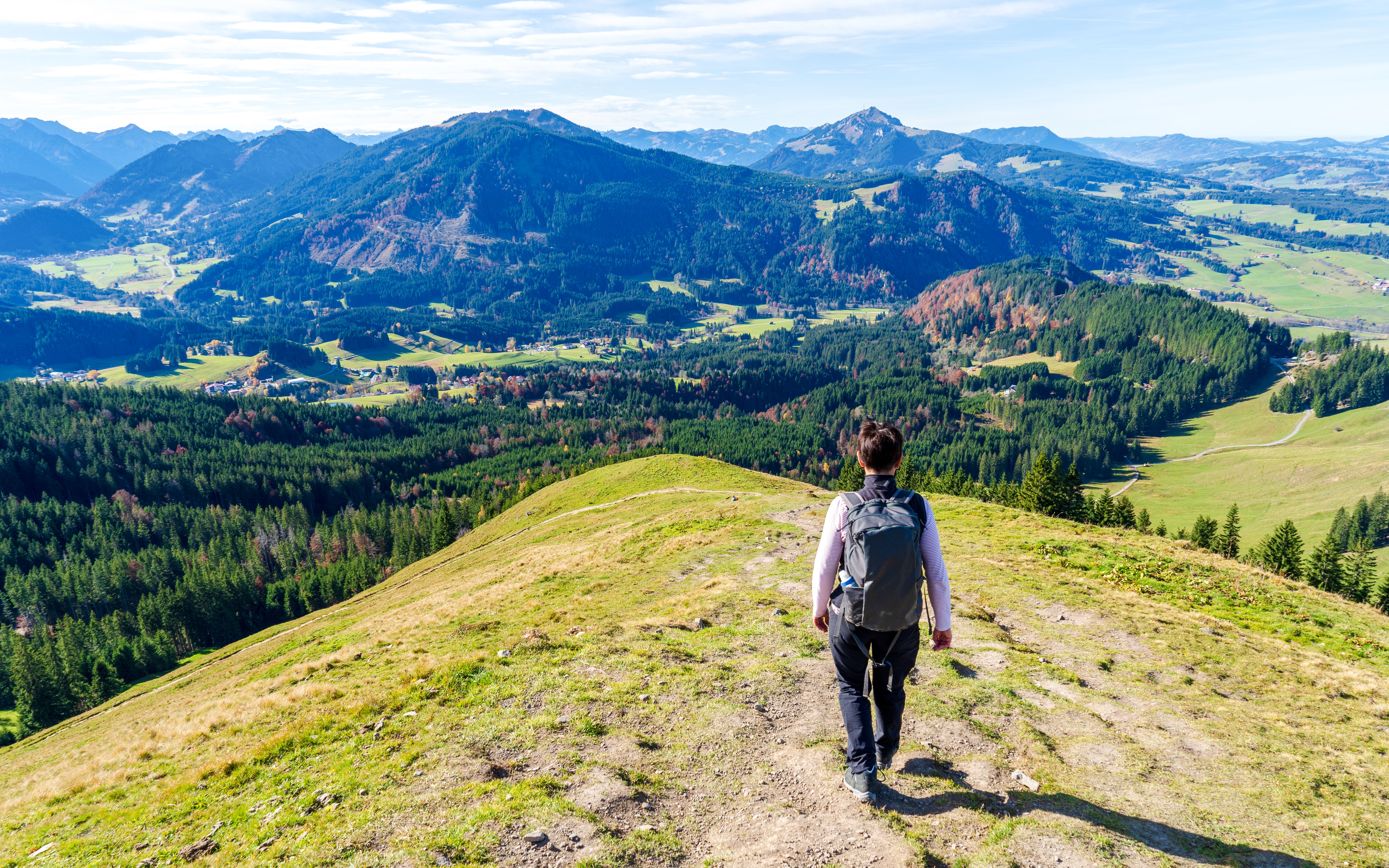 Hiker on Neuschwanstein Forest Trails overlooking lush valleys and distant mountains.